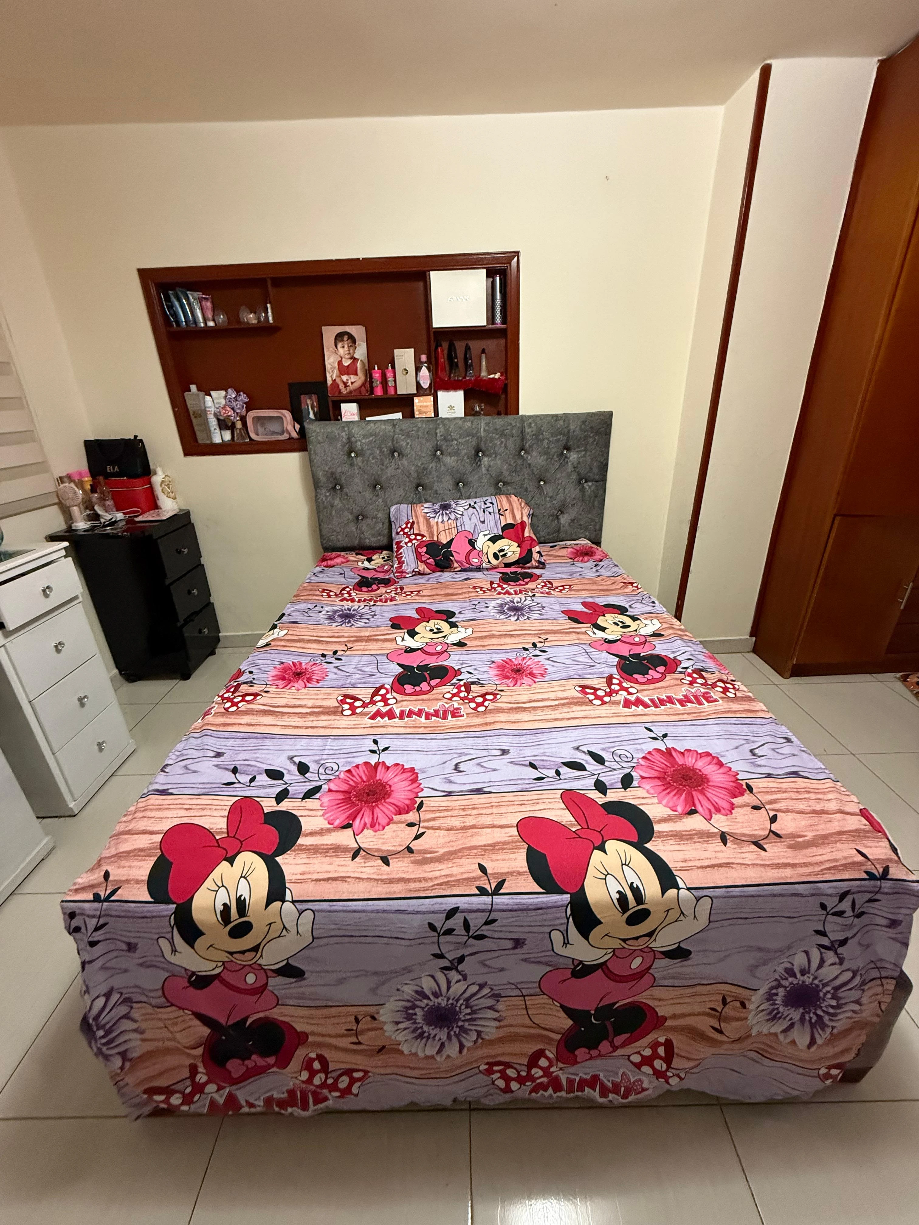 Sábana infantil piel de durazno con estampado de Minnie Mouse, colocada sobre cama con cabecero tapizado gris.