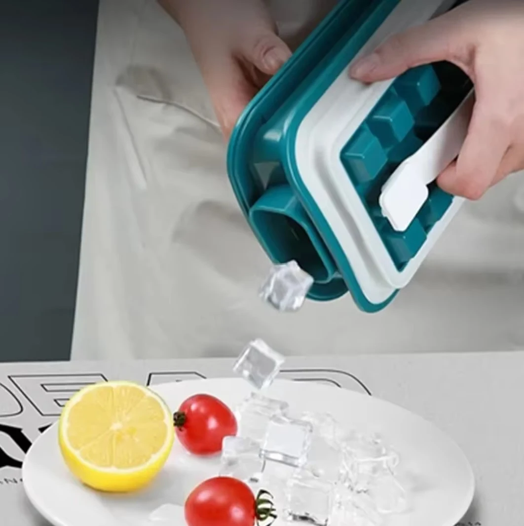 Molde de silicona verde y blanco para cubos de hielo, liberando cubos sobre plato con limón y tomates.