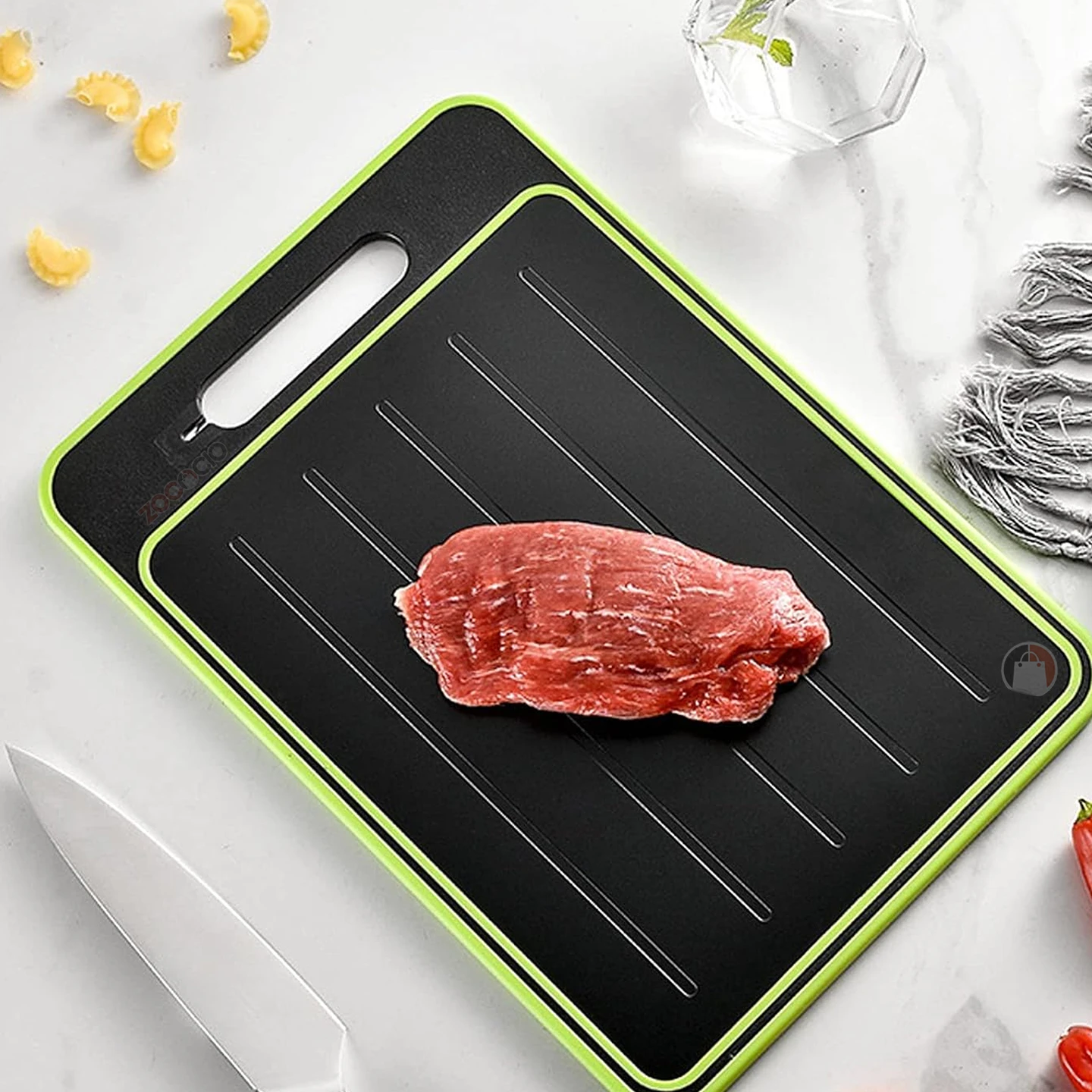 Tabla de corte negra con borde verde lima, superficie texturizada con líneas paralelas y mango integrado, mostrando una porción de carne cruda en el centro.