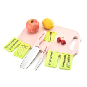 Tabla de cortar rosa con colador integrado y cinco cuchillas intercambiables, acompañada de manzanas, limón y cerezas.