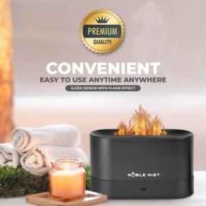 Difusor ultrasónico Noble Mist negro con llama LED realista, acompañado de toallas blancas, vela encendida y musgo, sobre superficie clara.