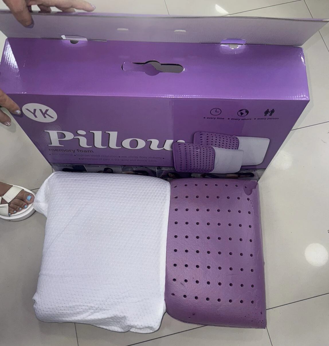 Almohada de espuma viscoelástica con funda blanca y base morada perforada, mostrada junto a su caja original de color lila.
