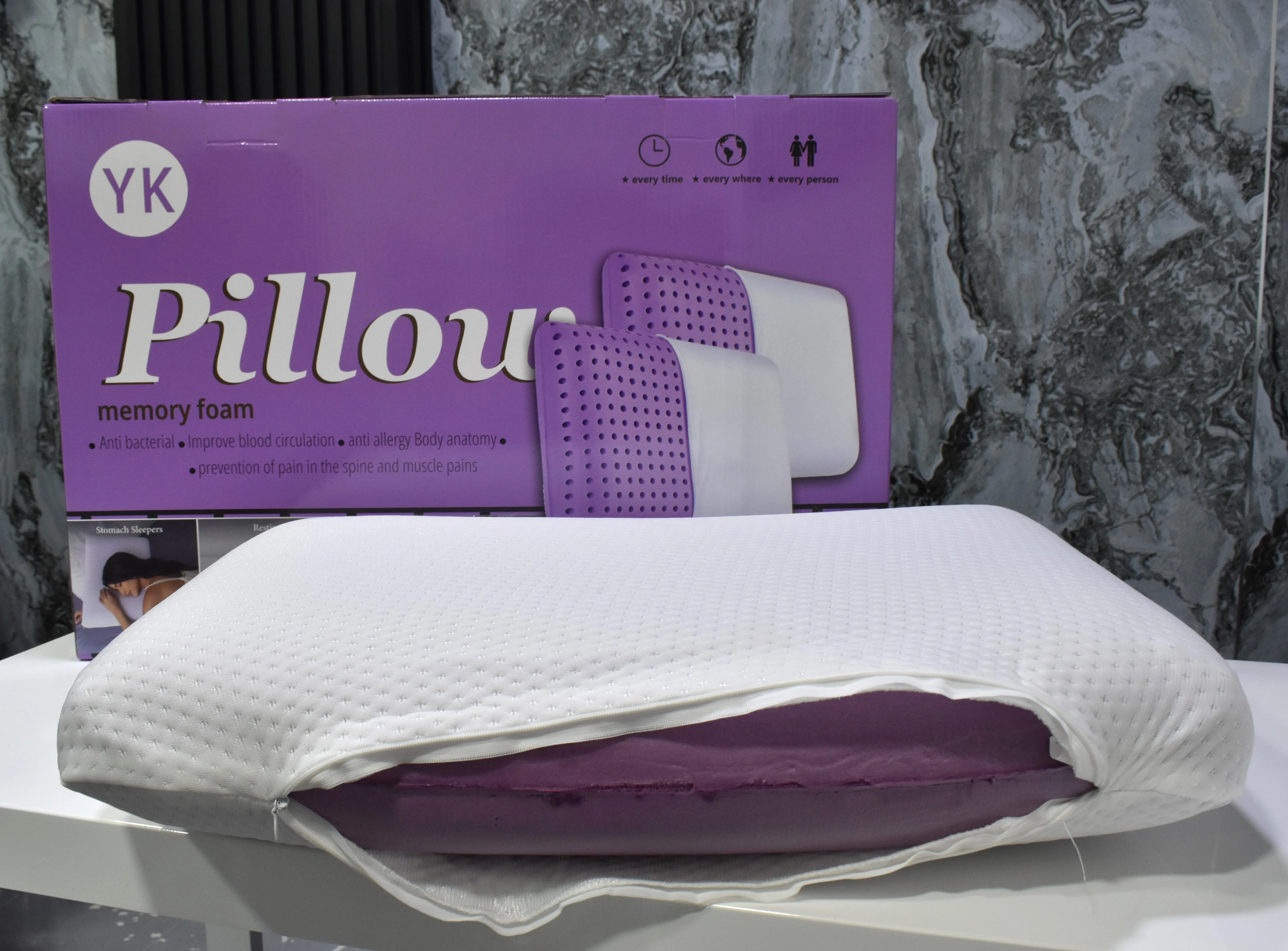 Almohada de espuma viscoelástica blanca con funda texturizada y relleno morado, exhibida junto a su caja púrpura con logotipo YK.