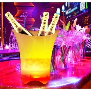 Cubeta hielera LED con luces multicolor, altavoz Bluetooth y tres botellas de Moët insertadas, sobre barra de bar con copas de champán.