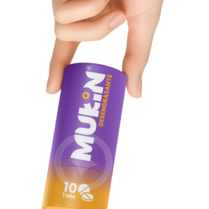 Mano sosteniendo un envase cilíndrico de Mukin Desengrasante con degradado de morado a naranja. La etiqueta muestra 10 Tabs y el nombre de la marca en letras blancas mayúsculas.