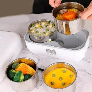 Lonchera eléctrica blanca con recipientes de acero inoxidable: arroz, sopa, verduras y huevo cocido.
