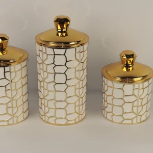 Juego de tres recipientes cilíndricos para cocina. Cuerpo blanco con patrón geométrico en relieve dorado y tapas redondas de color oro brillante con pomo facetado.
