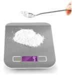 Balanza digital de cocina en acero inoxidable con pantalla LED mostrando 9 gramos, sobre la que se encuentra una pila de polvo blanco, mientras una mano sostiene una cuchara con más del mismo ingrediente encima.