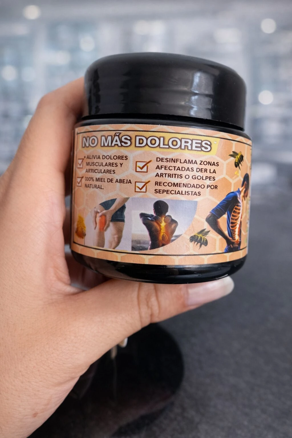Contenedor negro de crema Apitoxina para articulaciones, con etiqueta que muestra ilustraciones de personas aplicándola en zonas afectadas y texto sobre alivio de dolores musculares y articulares.