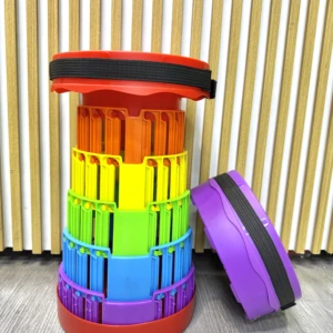 Silla plegable Acora Butaco desmontada, con piezas apiladas en colores rojo, naranja, amarillo, verde, azul y morado, junto a las tapas de transporte.
