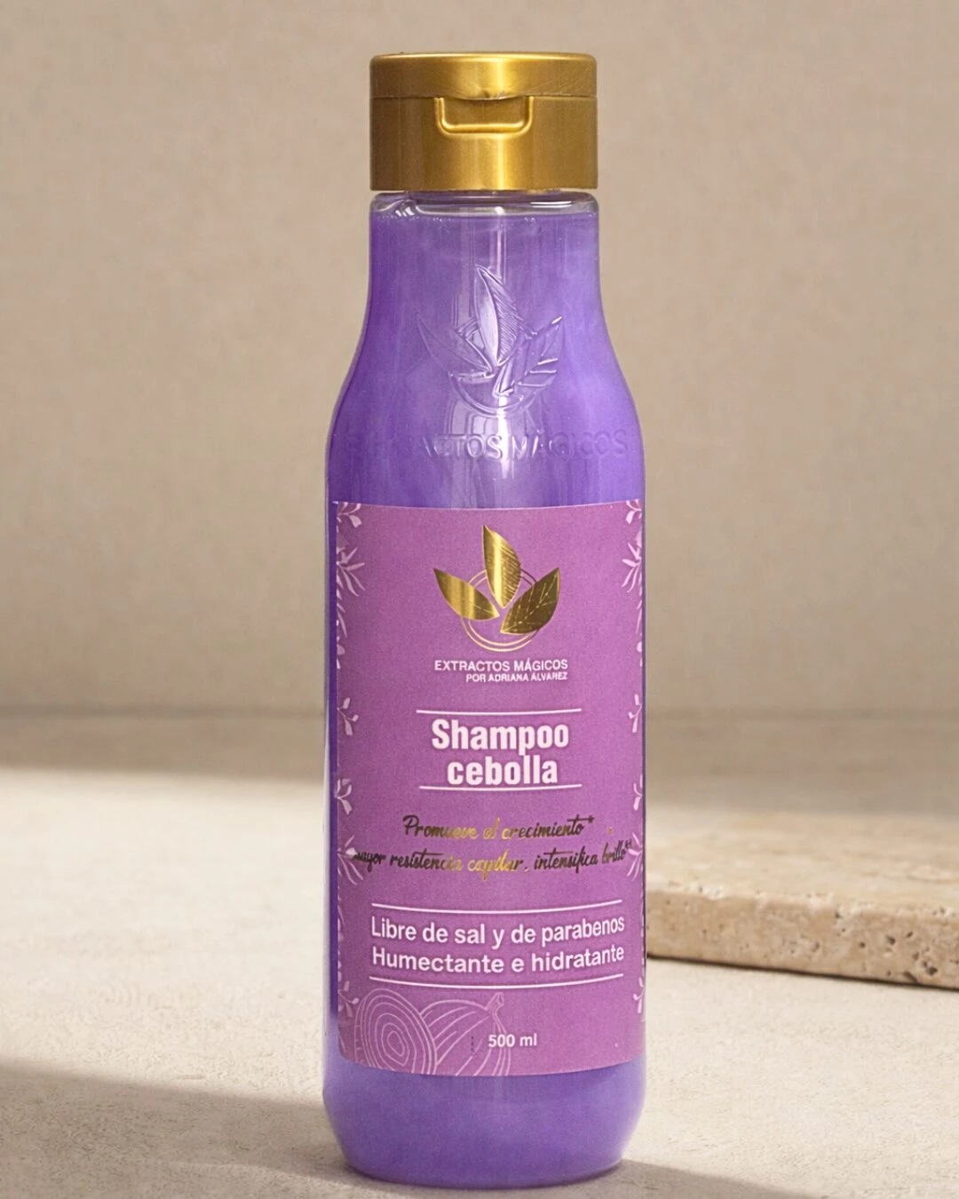 Bote de champú de cebolla para crecimiento capilar, color morado con tapa dorada, etiqueta que indica libre de sal y parabenos, humectante e hidratante.