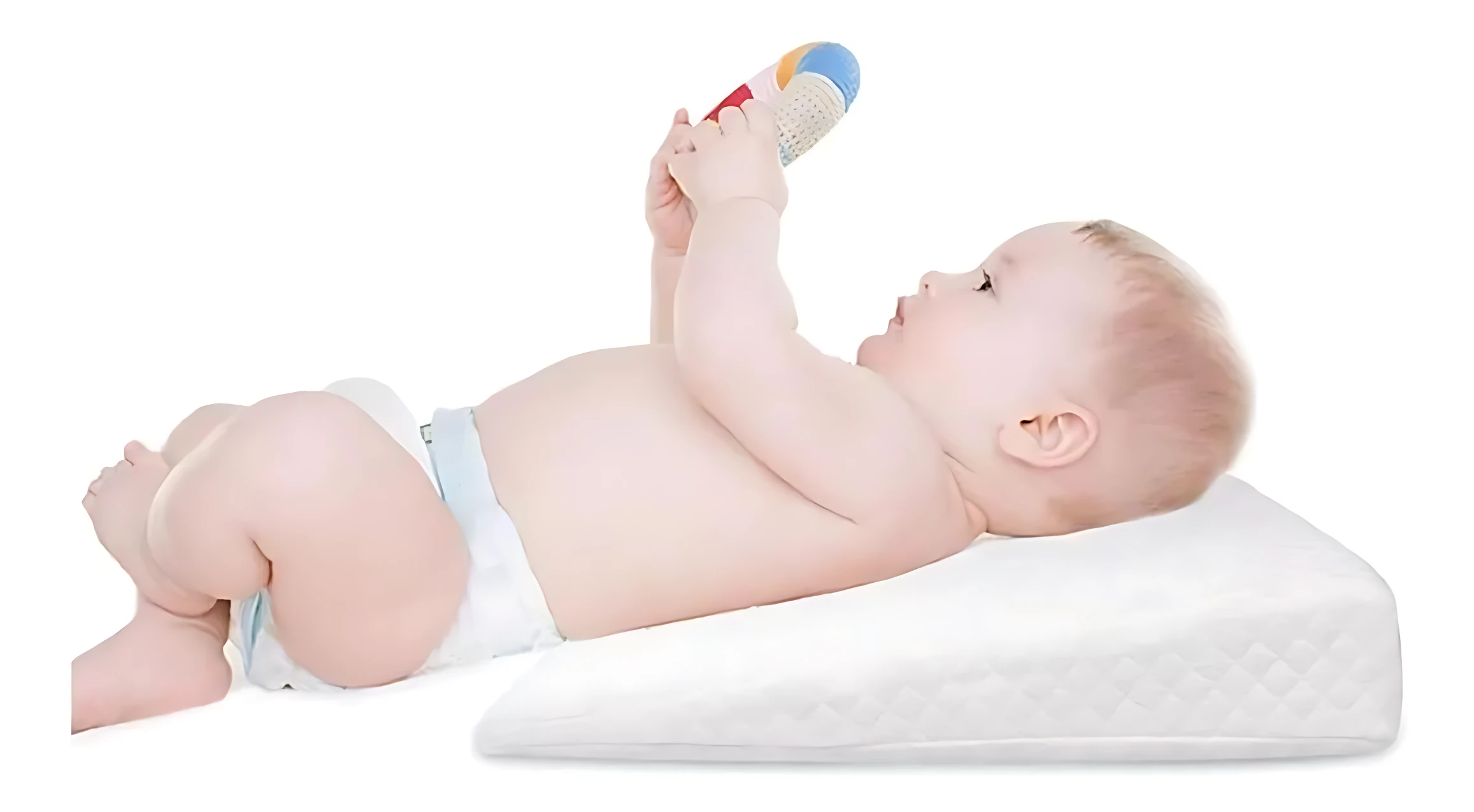 Bebé boca arriba jugando con sonajero sobre almohada antireflujo blanca inclinada para colecho.