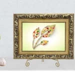 Soporte de exhibición dorado con marco ornamental y base de hierro, mostrando cuadro floral sobre fondo claro, acompañado de jarrones decorativos a la izquierda.