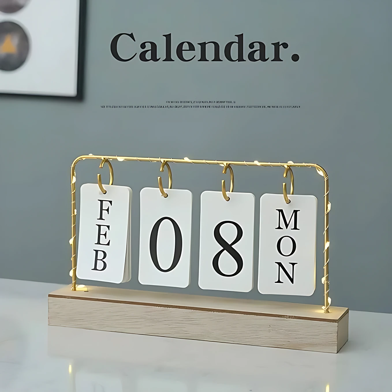 Calendario de escritorio con base de madera clara y marco dorado con luces LED. Muestra fichas blancas indicando la fecha 08 de febrero y el día lunes. Diseño minimalista para decoración.