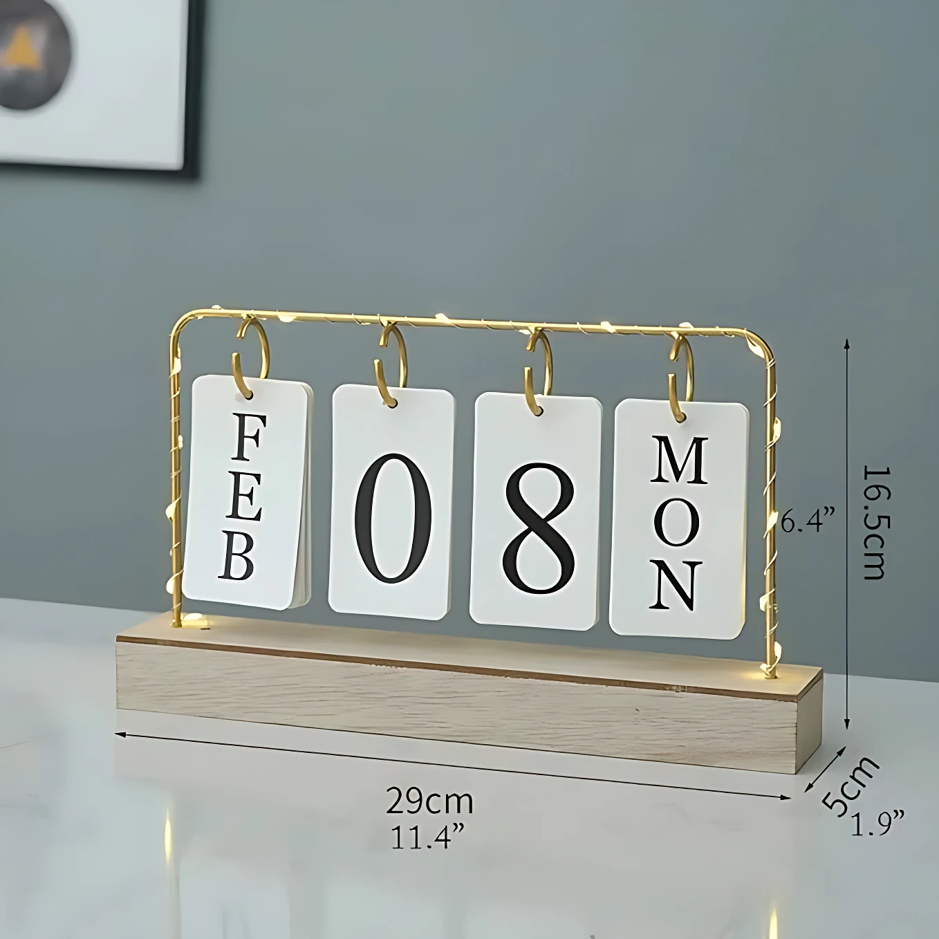 Calendario de escritorio con base de madera clara y marco dorado con luces LED. Muestra las fechas FEB 08 MON. Medidas visibles: 29cm de largo, 16.5cm de alto y 5cm de profundidad. Diseño minimalista para decoración de interiores.
