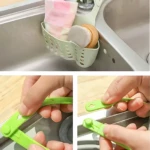 Canasta escurridora verde de plástico colgante para fregadero con esponja y paños.