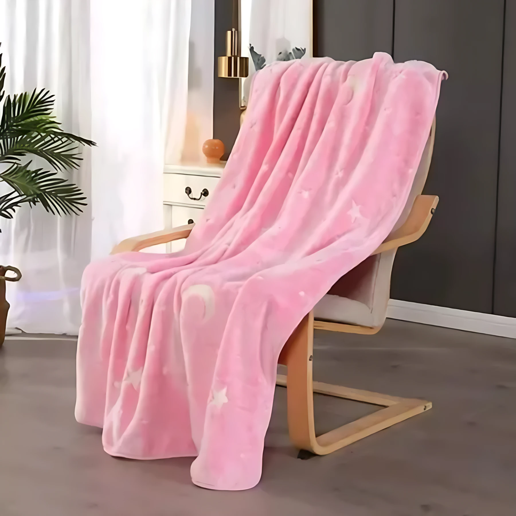 Cobija rosa de felpa con estampado de estrellas y lunas blancas, colocada sobre una silla de madera en una habitación con luz natural.