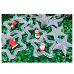 Cortina de luces LED en forma de estrellas con efecto tornasol y figuras navideñas colgantes como Santa, renos y muñeco de nieve sobre fondo verde.