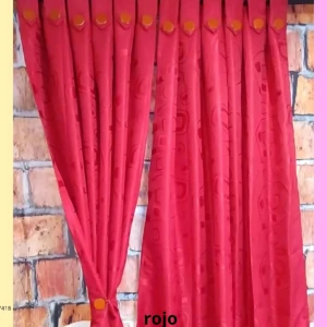 Cortina Yakar en color rojo con patrón textil sutil, colgada frente a pared de ladrillo visto. Incluye botones decorativos dorados en la parte superior.