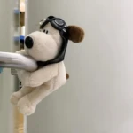Peluche perro blanco con gafas de piloto negro, sujetado a barra metálica plateada.