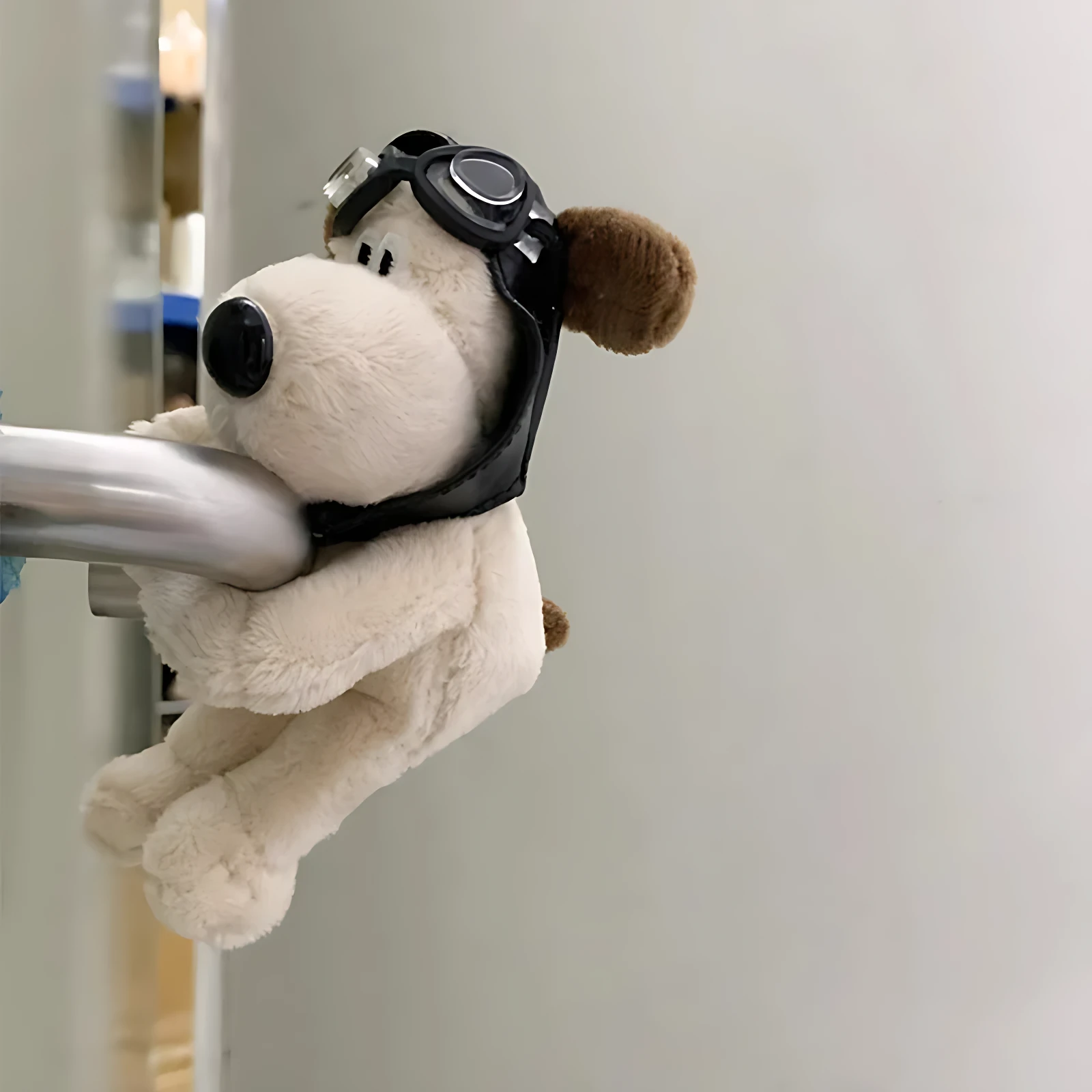 Peluche perro blanco con gafas de piloto negro, sujetado a barra metálica plateada.