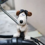 Peluche perro blanco con gafas de piloto, sentado en el manillar de una motocicleta.