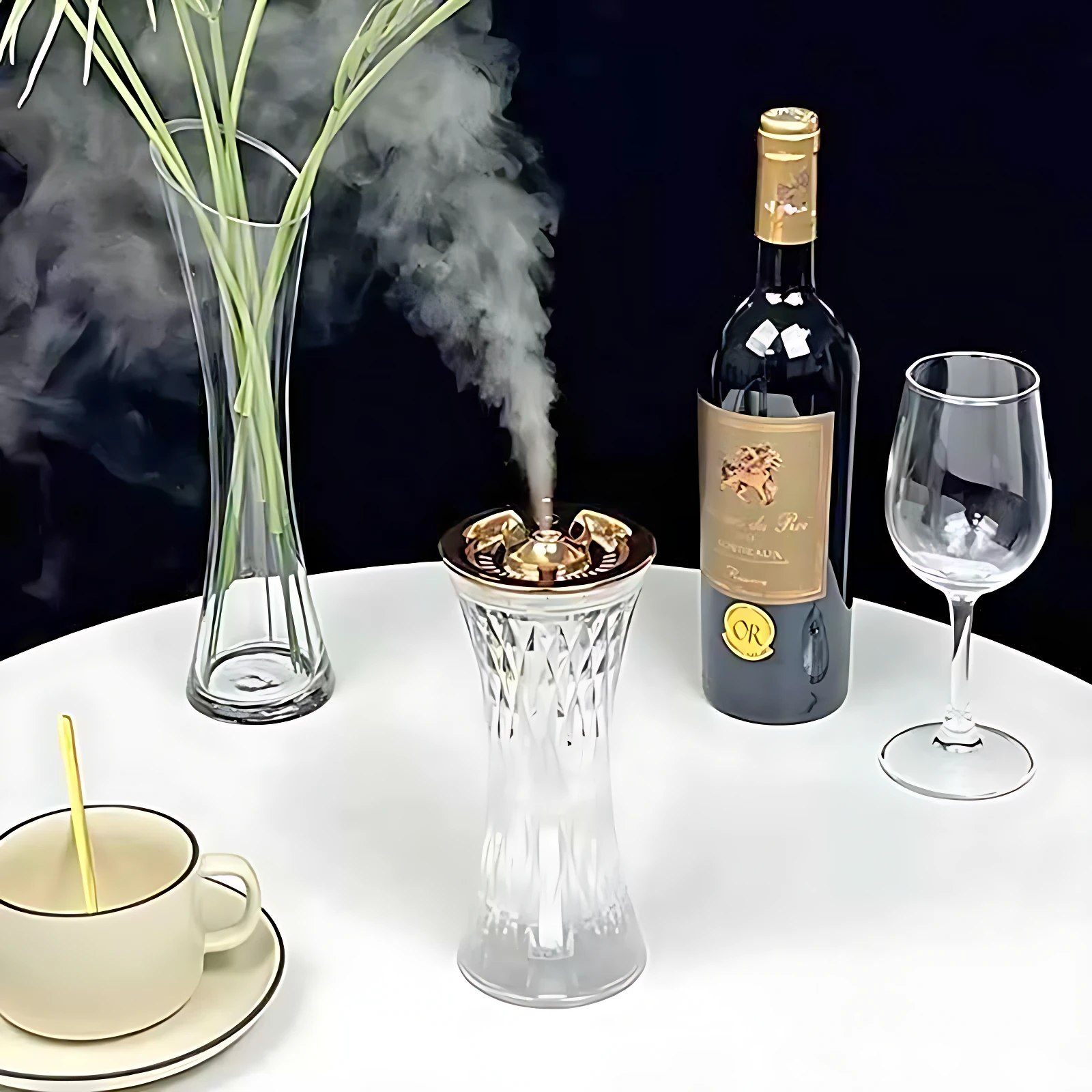 Difusor aroma jarra de cristal con luz LED, emitiendo vapor sobre mesa blanca junto a botella de vino y copa.