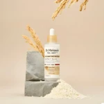 Ampolla facial Dr.Melaxin Peel Shot con arroz blanco y niacinamida, sobre pedestal de concreto, rodeada de arroz y espigas.