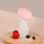 Extractor de leche materna manual en silicona rosa con tapa, sobre tabla de madera con fresas y arándanos.