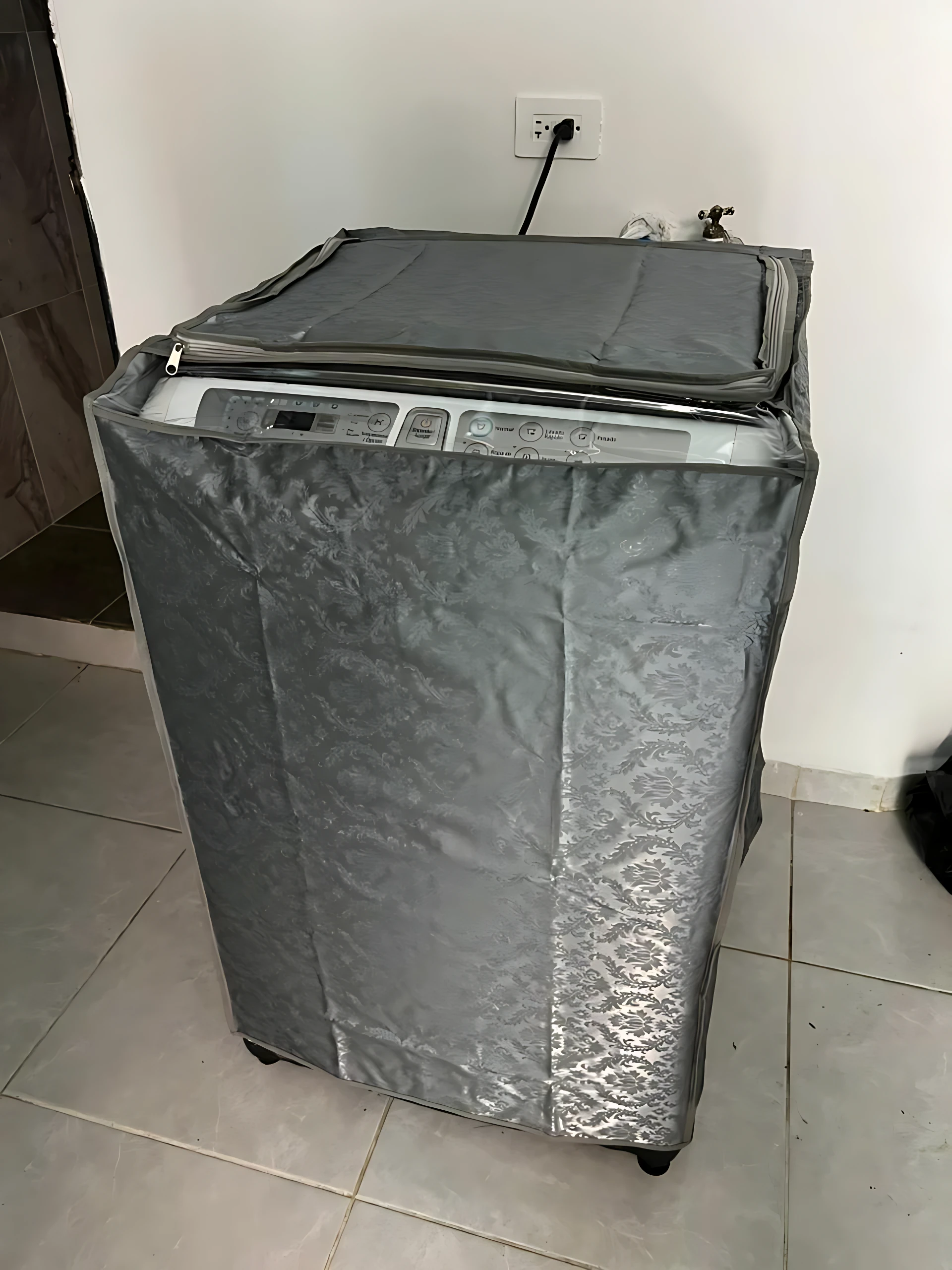 Forro protector gris para lavadora frontal, con cierre superior y paneles laterales acolchados, instalado sobre electrodoméstico en ambiente doméstico.