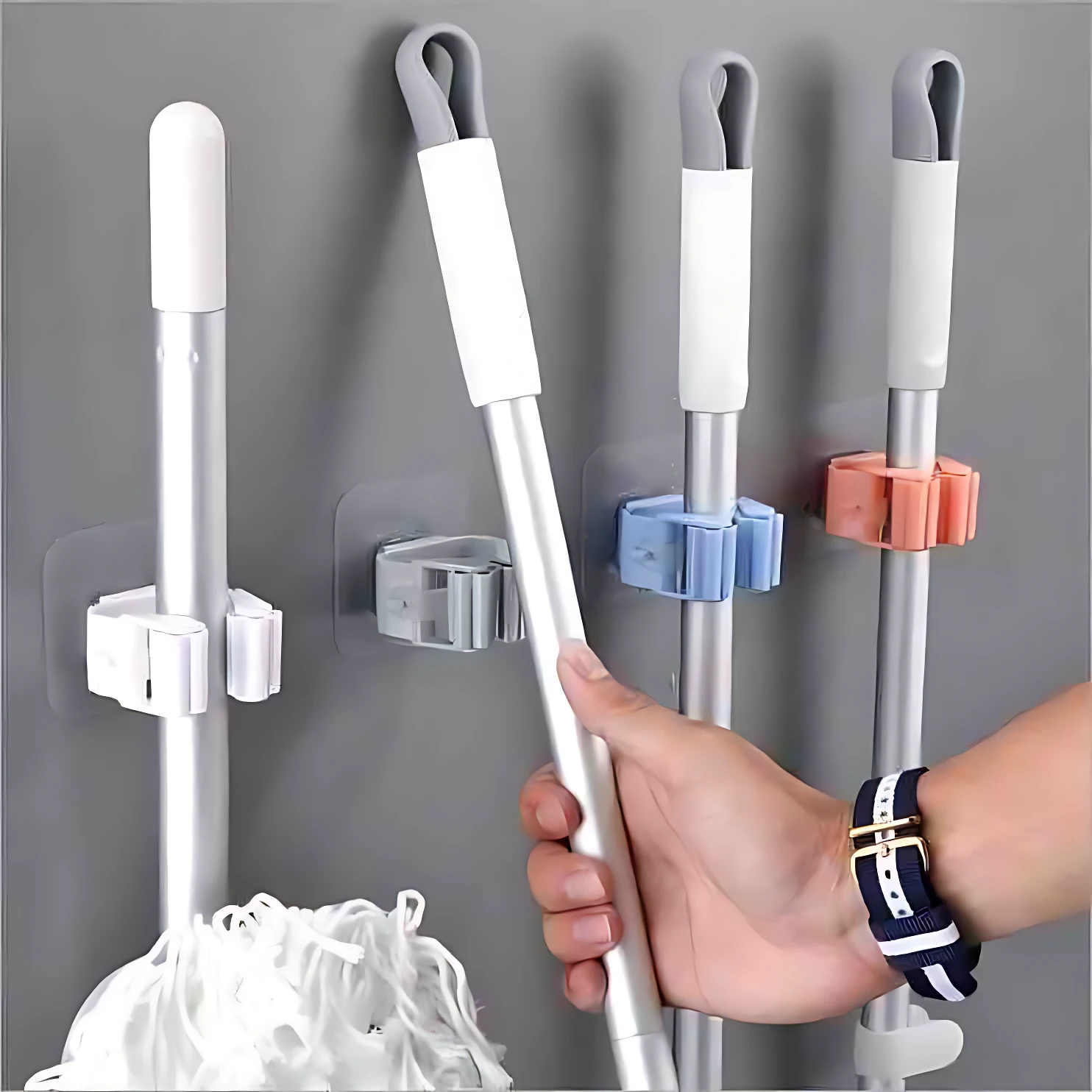 Ganchos adhesivos resistentes, en gris, azul, rosa y blanco, para organizar escobas y trapeadores en la pared.