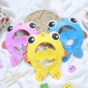 Tres gorros de baño para niños en colores rosa, amarillo y azul, con diseño de pato y ojos grandes, dispuestos sobre tela blanca junto a accesorios de manualidades.