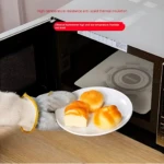 Guantes de alambre de acero para microondas, protegen del calor, con panecillos en plato blanco.