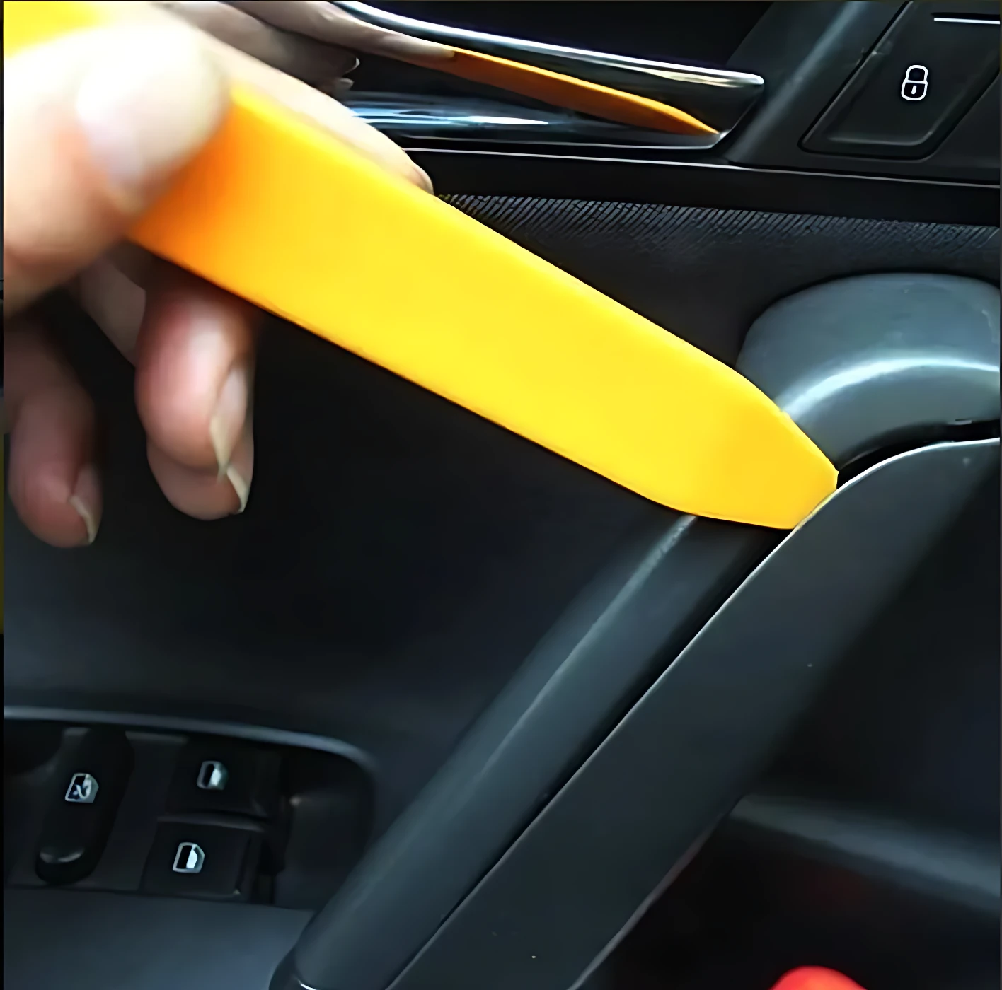 Herramienta plástica amarilla extrae molduras de puerta de auto sin rayar, vista en uso con mano sosteniendo el mango.
