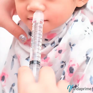 Jeringa nasal transparente con marcas de medida, siendo usada por un adulto para administrar solución en la nariz de un bebé con pañuelo floral.