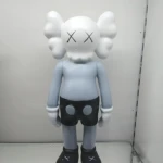 Figura decorativa de resina estilo KAWS, 18 cm, color gris claro con detalles negros y ojos en X, sobre fondo blanco.