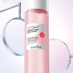 Tónico facial Sadoer Pink Salt con centella, 100ml, en frasco rosa, rodeado de soportes metálicos.