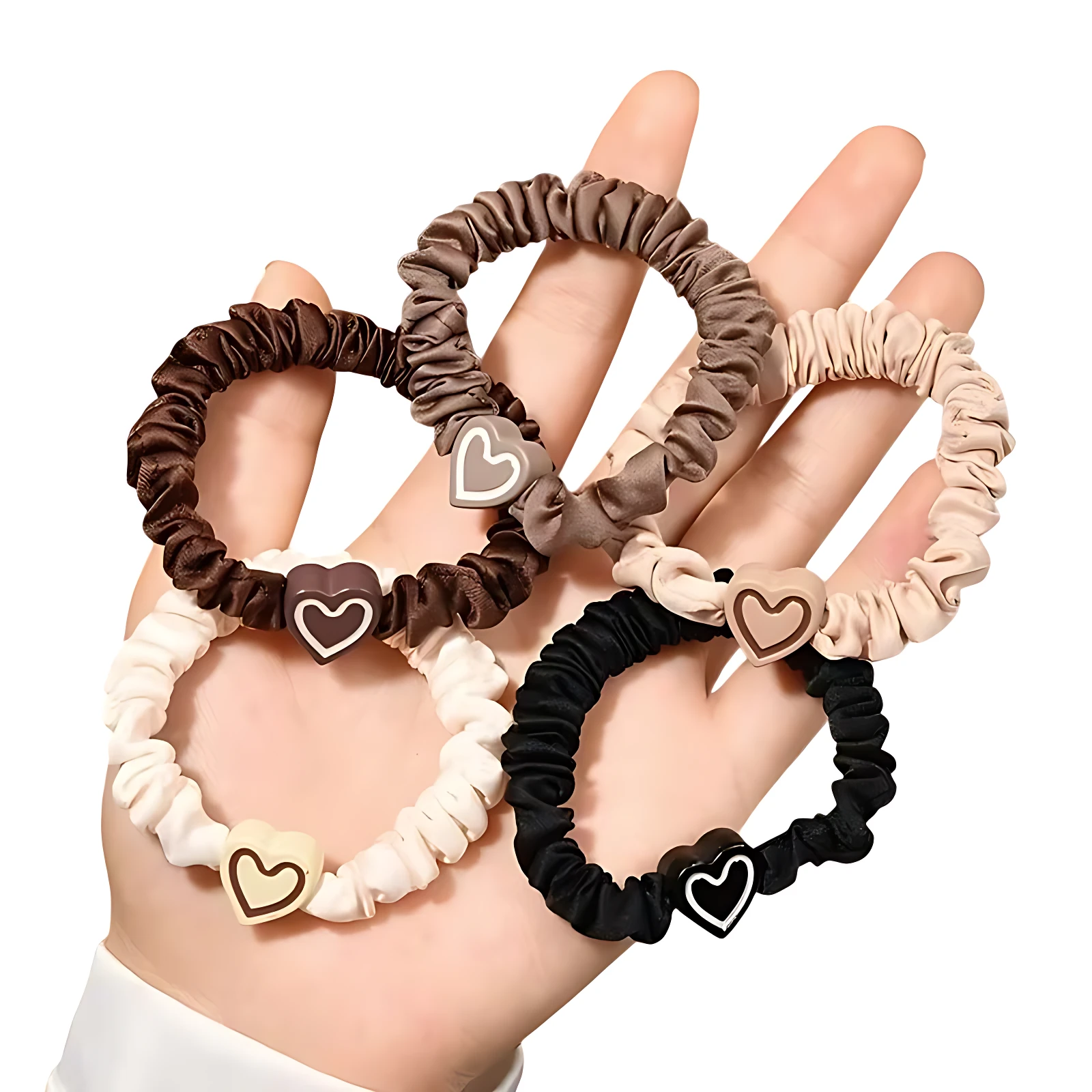 Ligas para cabello de seda en tonos tierra y negro con dijes de corazón, presentadas en una mano.
