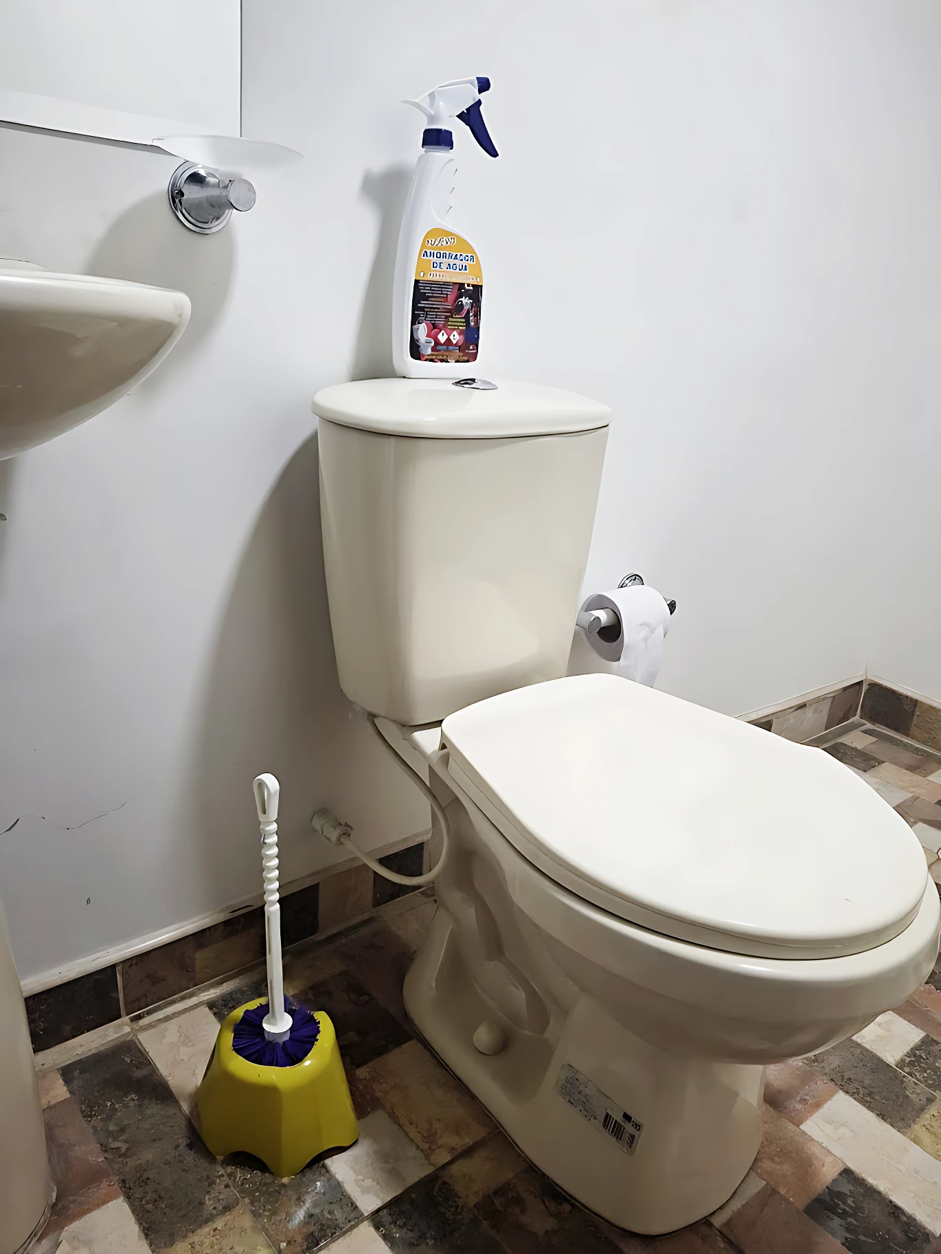Inodoro blanco con tapa cerrada, junto a inodoro de baño con brocha amarilla y botella de limpiador sobre el tanque.