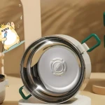 Lonchera térmica de 2 niveles, acero inoxidable, con asas verdes, diseño moderno y caricatura de gato en fondo beige.