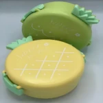 Lonchera térmica en forma de piña, disponible en amarillo y verde, con diseño de pino y detalles en blanco. Ideal para llevar comidas frescas y seguras.