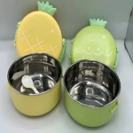 Lonchera térmica de acero inoxidable con tapa de piña en amarillo y verde, mostrando interior metálico y cuchara blanca en modelo amarillo.