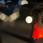 Set x2 luces LED rojas en forma de corazón para bicicleta, colgadas bajo el sillín, con fondo de luces nocturnas difuminadas.