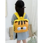 Mochila amarilla con diseño de tigre, vista trasera en niña con gorra negra, sobre fondo blanco con cojines y botellas en canasta.