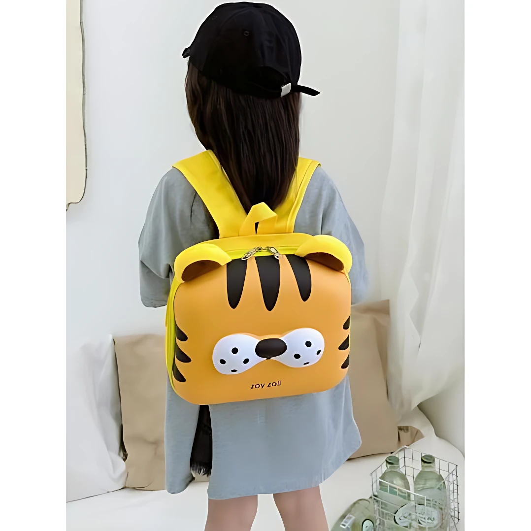Mochila amarilla con diseño de tigre, vista trasera en niña con gorra negra, sobre fondo blanco con cojines y botellas en canasta.