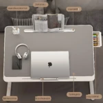 Mesa de escritorio plegable color gris con laptop, audífonos, cuaderno y ventilador USB integrado, ideal para trabajar o estudiar en cualquier lugar.