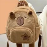Mochila escolar infantil de felpa color beige con diseño de capibara kawaii, frente visible, bolsillo frontal con estrella bordada.