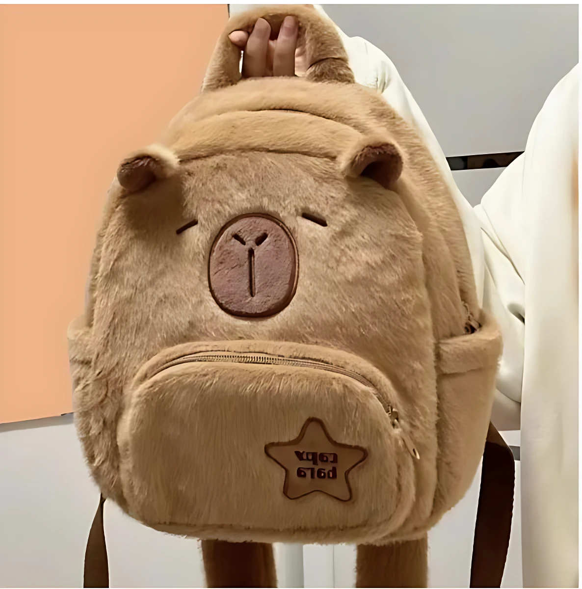 Mochila escolar infantil de felpa color beige con diseño de capibara kawaii, frente visible, bolsillo frontal con estrella bordada.