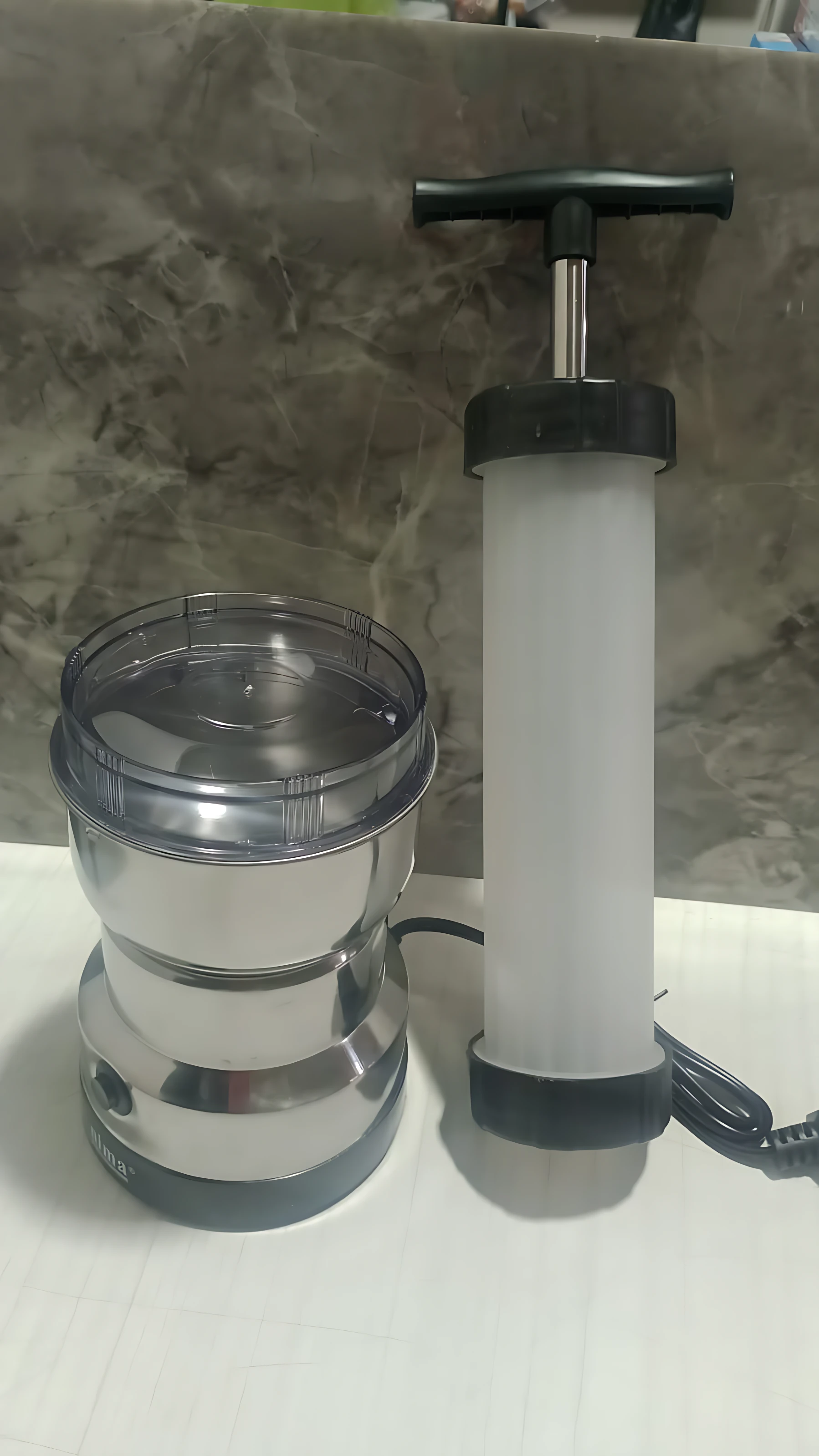 Molino de café y embutidora de salchicha con base metálica y accesorio de bombeo blanco, sobre superficie clara.