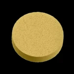 Tableta circular de color beige con textura granulada y poros visibles, vista superior con sombra, producto desengrasante efervescente Mukin.